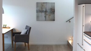 Et minimalistisk værelse med trægulv, en grå stol, et hvidt skab og et billede på væggen.