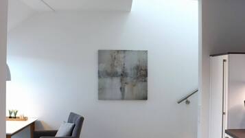 A minimalist room with a wooden floor, a grey chair, a white cabinet, and a painting on the wall.