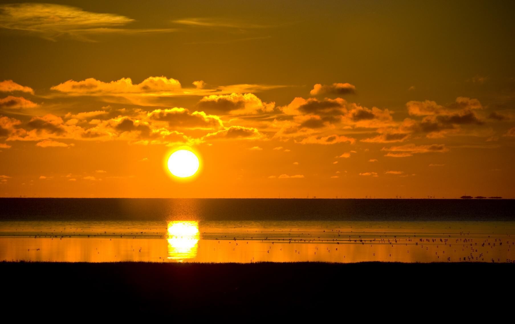 A sunset over a calm sea with a clear sky.