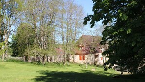 A house with a red roof, surrounded by a stone wall and trees.