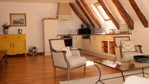A cozy loft-style living space with exposed wooden beams, a kitchen with white cabinets, and a dining area with a glass table.