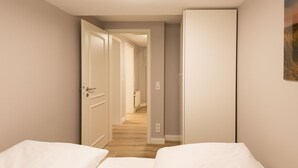 Una camera d'albergo con due letti, un corridoio che porta al bagno e una porta che dà su un'altra stanza.