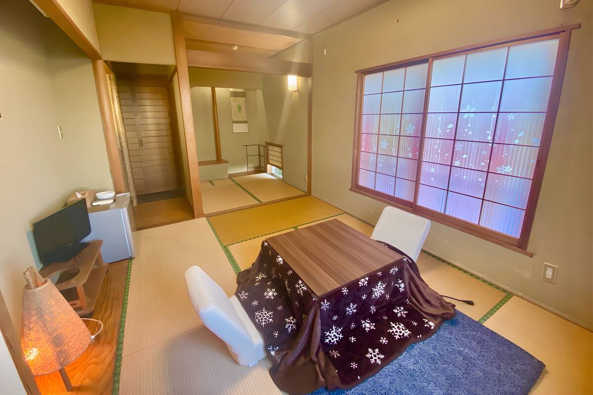 Una habitación japonesa tradicional con suelo de tatami, una mesa baja y una ventana con pantalla shoji.