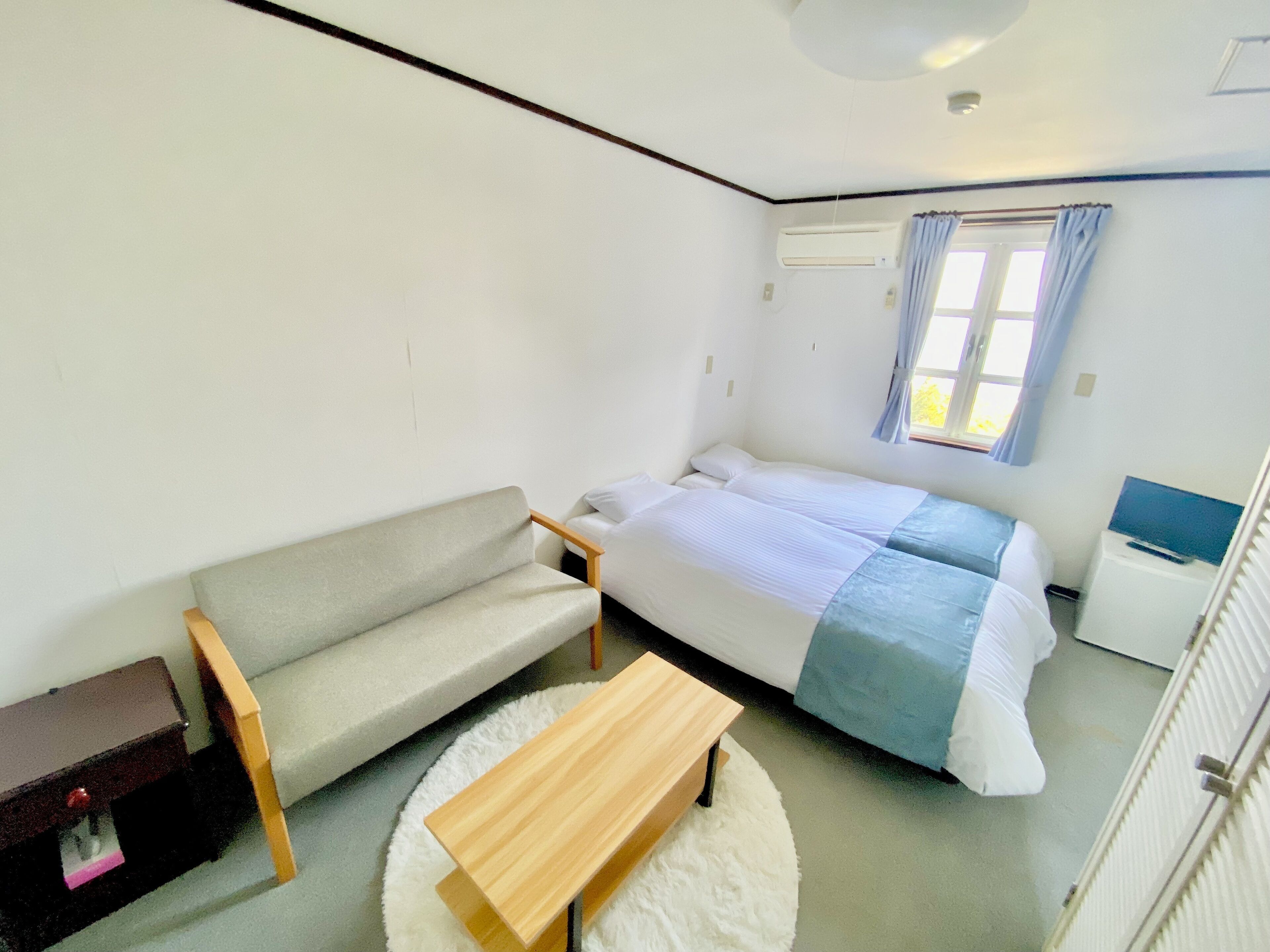 A room with a bed, a sofa, a small table, and a window with curtains.