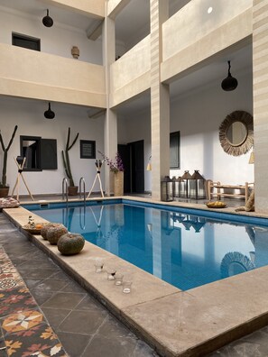 A modern indoor swimming pool with clear blue water, surrounded by a tiled deck and stone flooring.