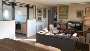 En stue med sofa, fjernsyn og bogreol. I forgrunden ses et spisebord med stole.