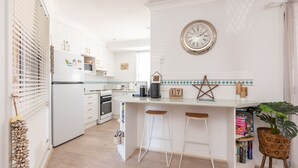 A modern kitchen with white cabinetry, a central island with stools, a clock on the wall, and a star decoration.