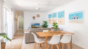 A modern living room with a sofa, dining table, and chairs, a television, and beach-themed wall art.