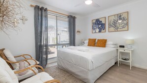 A bedroom with a bed, bedside table, lamp, and a view of the outdoors through the window.