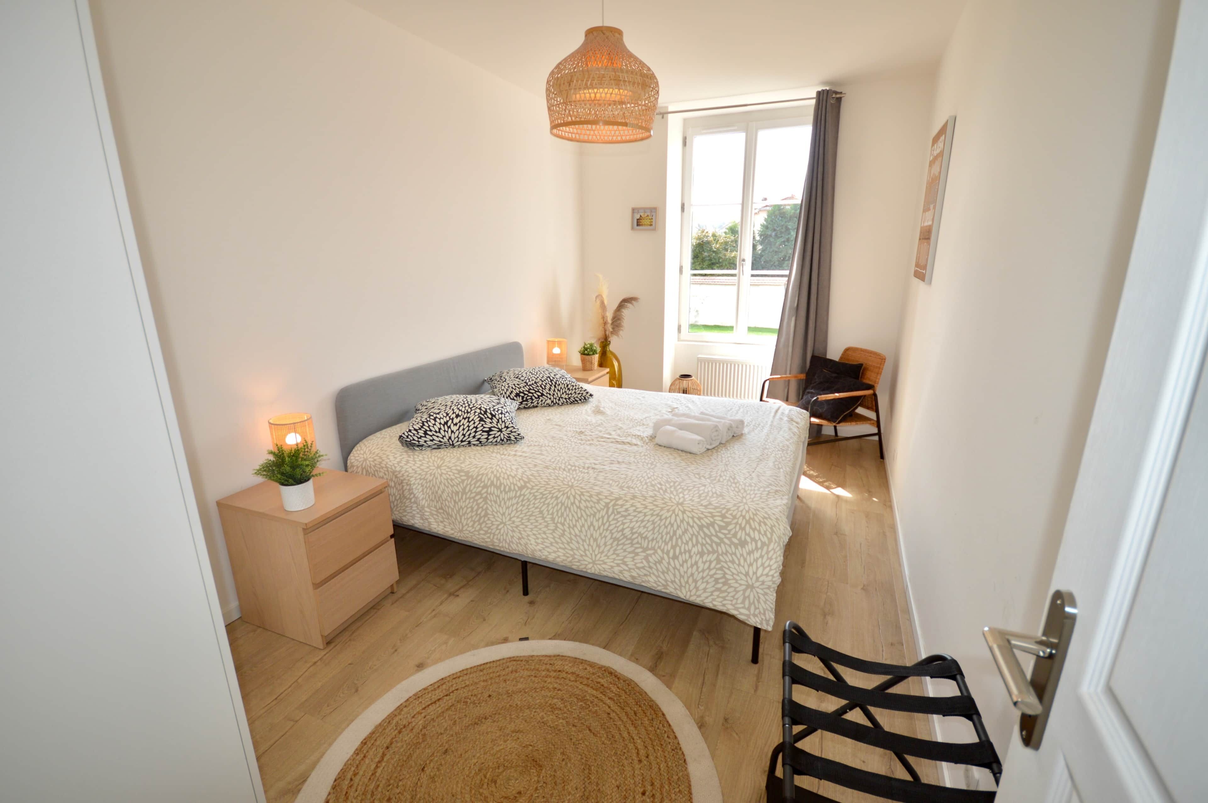Une chambre à coucher avec un lit, une table de chevet, une lampe et une vue sur l’extérieur.