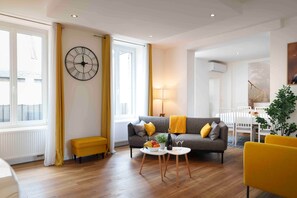 A modern living room with a sofa, a coffee table, a yellow bench, and a large wall clock.