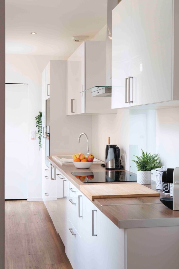A modern kitchen with white cabinets, a wooden countertop, a sink, a kettle, and a potted plant.