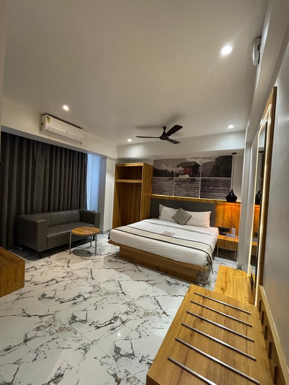 A modern hotel room with a bed, a sofa, a small table, and a wooden side table.
