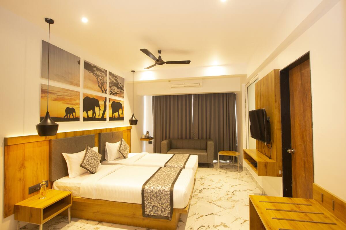 A hotel room with a large bed, a sofa, a TV, and artwork on the wall.