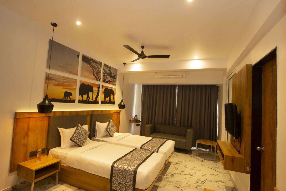 A hotel room with a bed, bedside tables, a sofa, a TV, and artwork on the wall.