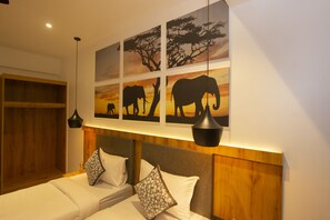 Un dormitorio con dos camas, cabeceros de madera y una pared decorada con cuatro cuadros de elefantes.