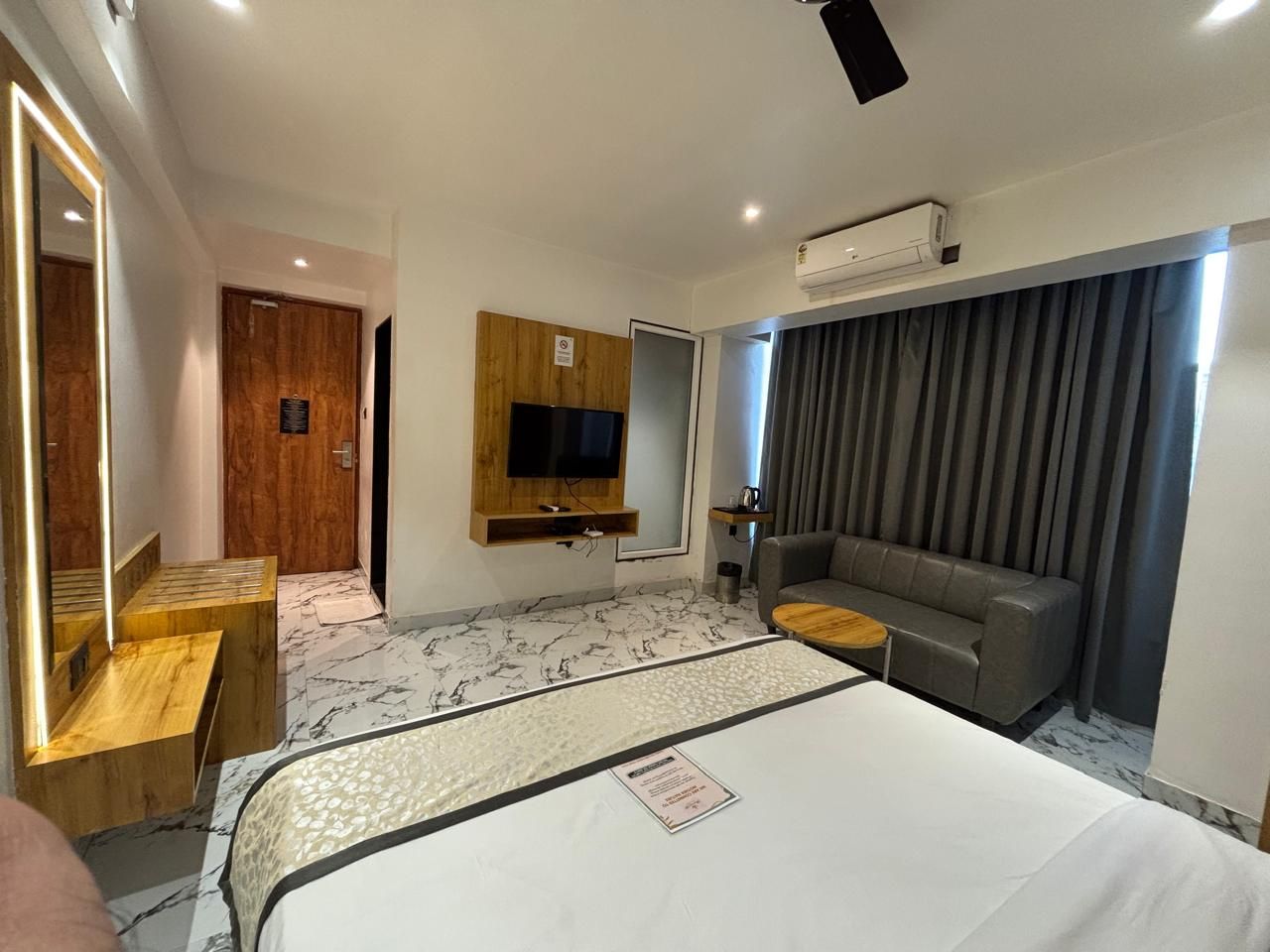 A hotel room with a bed, a sofa, a TV, and a wooden bench.