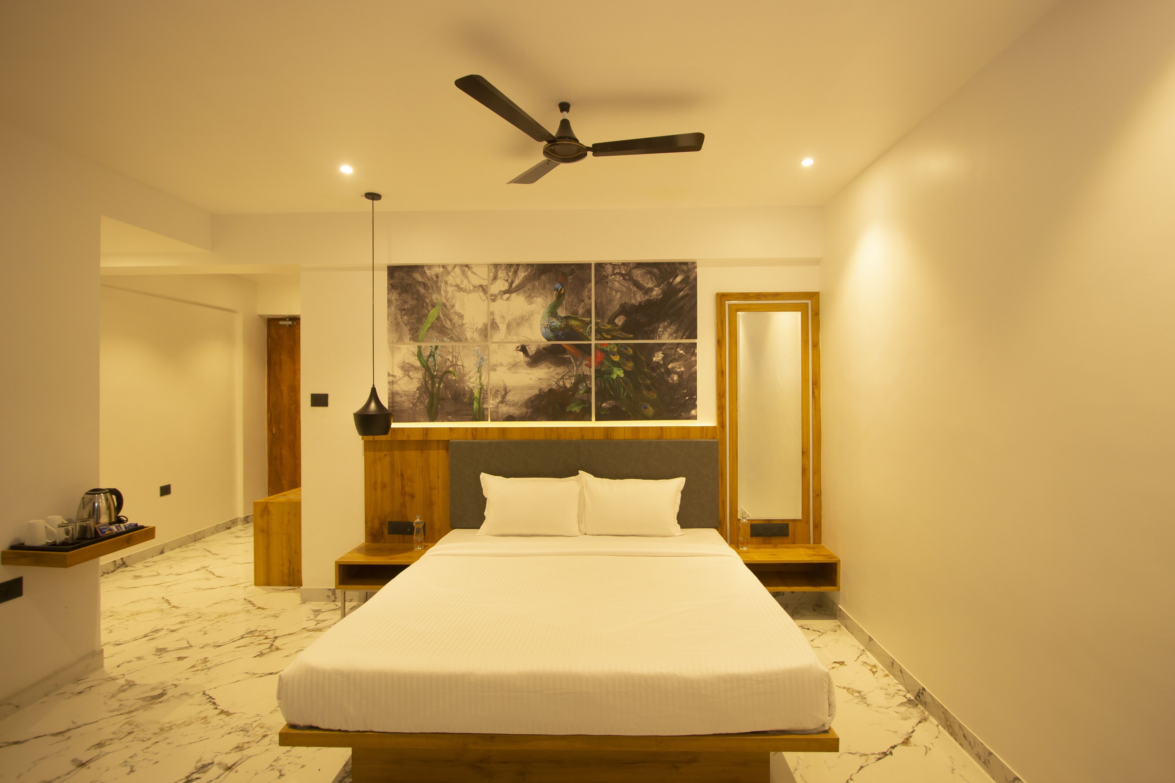 A modern bedroom with a large bed, a ceiling fan, a nightstand, a bedside table, and a wall-mounted artwork.