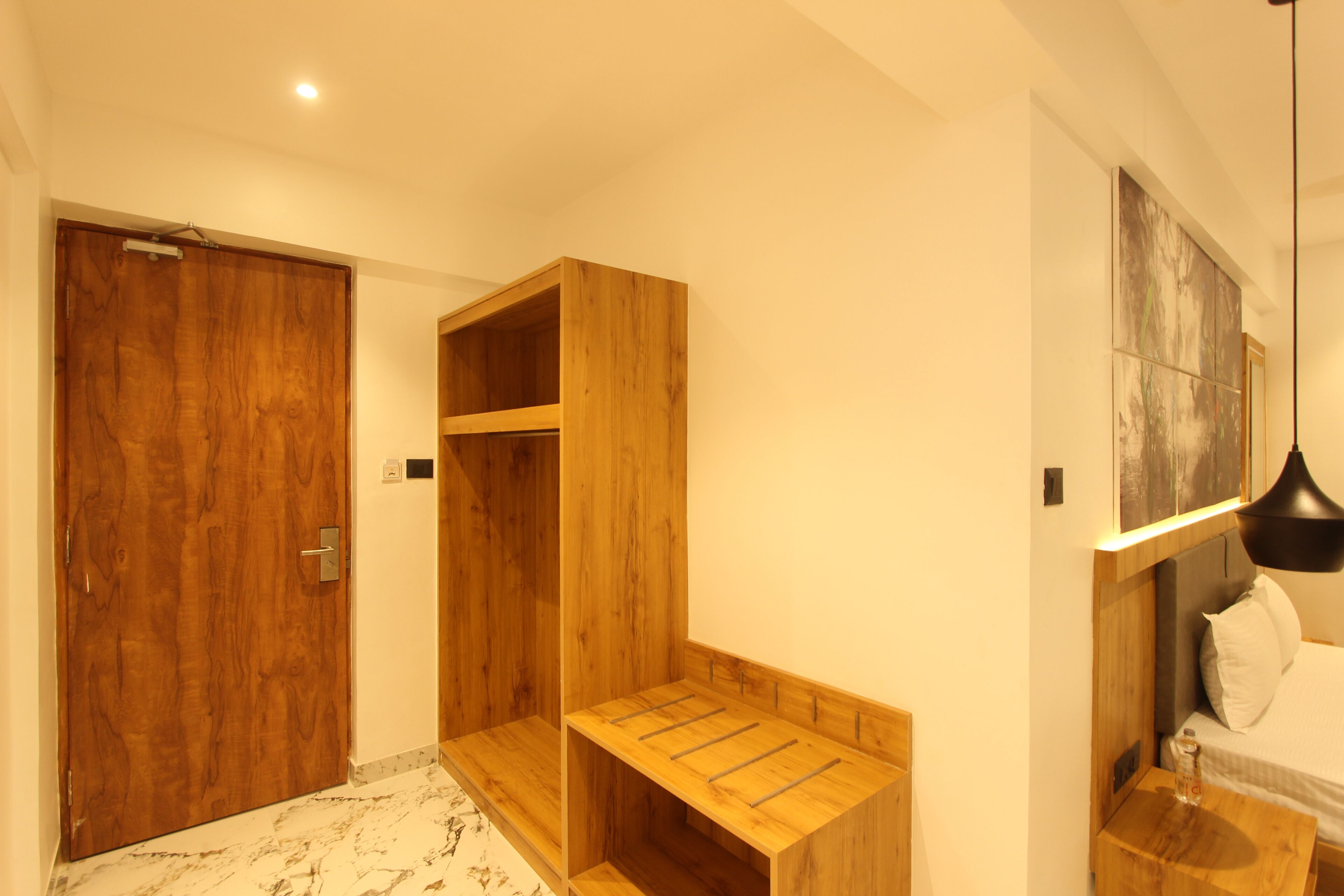 A bedroom with a wooden wardrobe, a wooden bench, a bed with white bedding, and a modern pendant light.