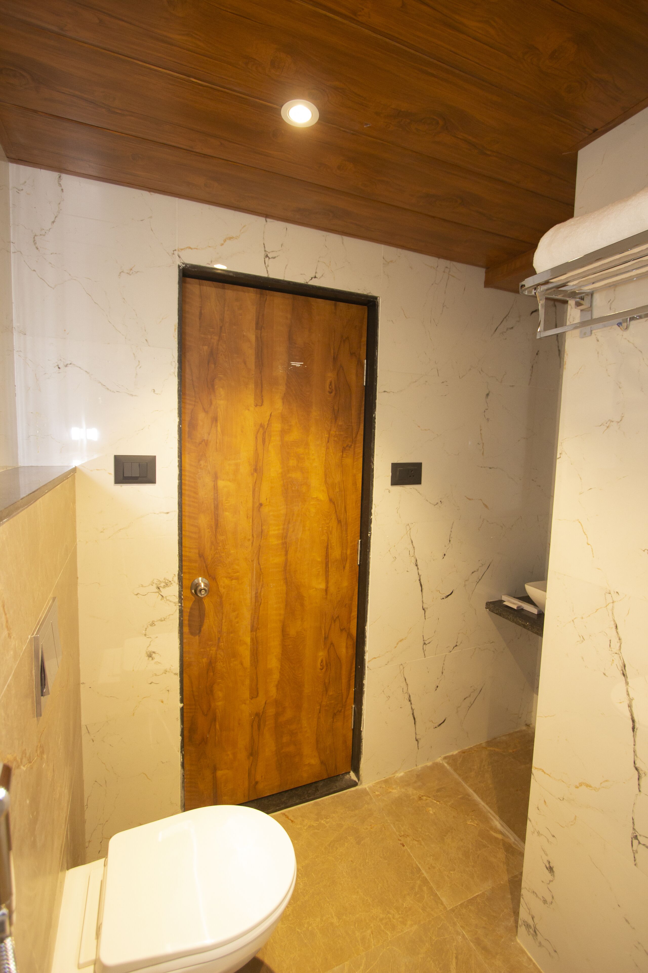 A bathroom with a wooden door, marble walls, and a toilet.