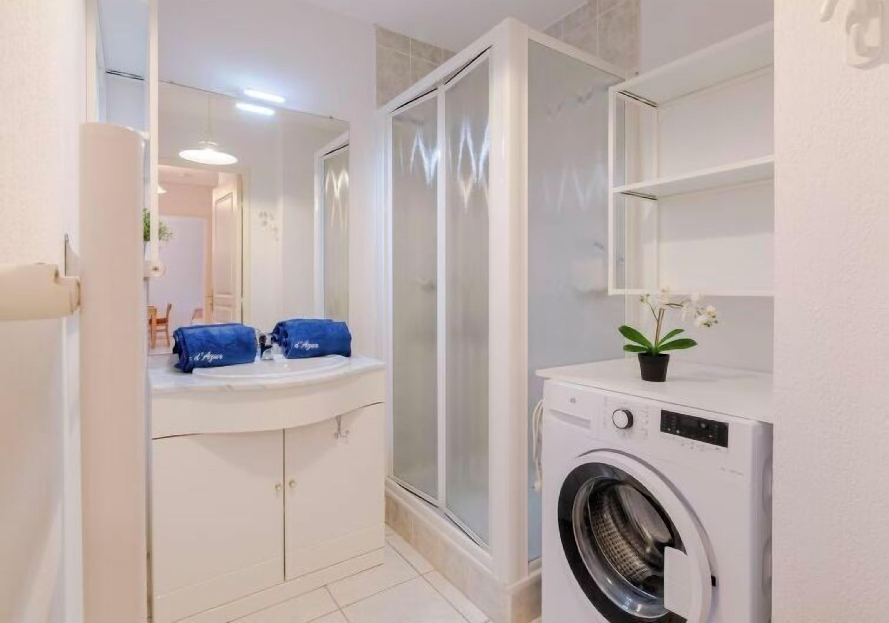 A compact bathroom with a washing machine, a shower enclosure, and a sink with a mirror.