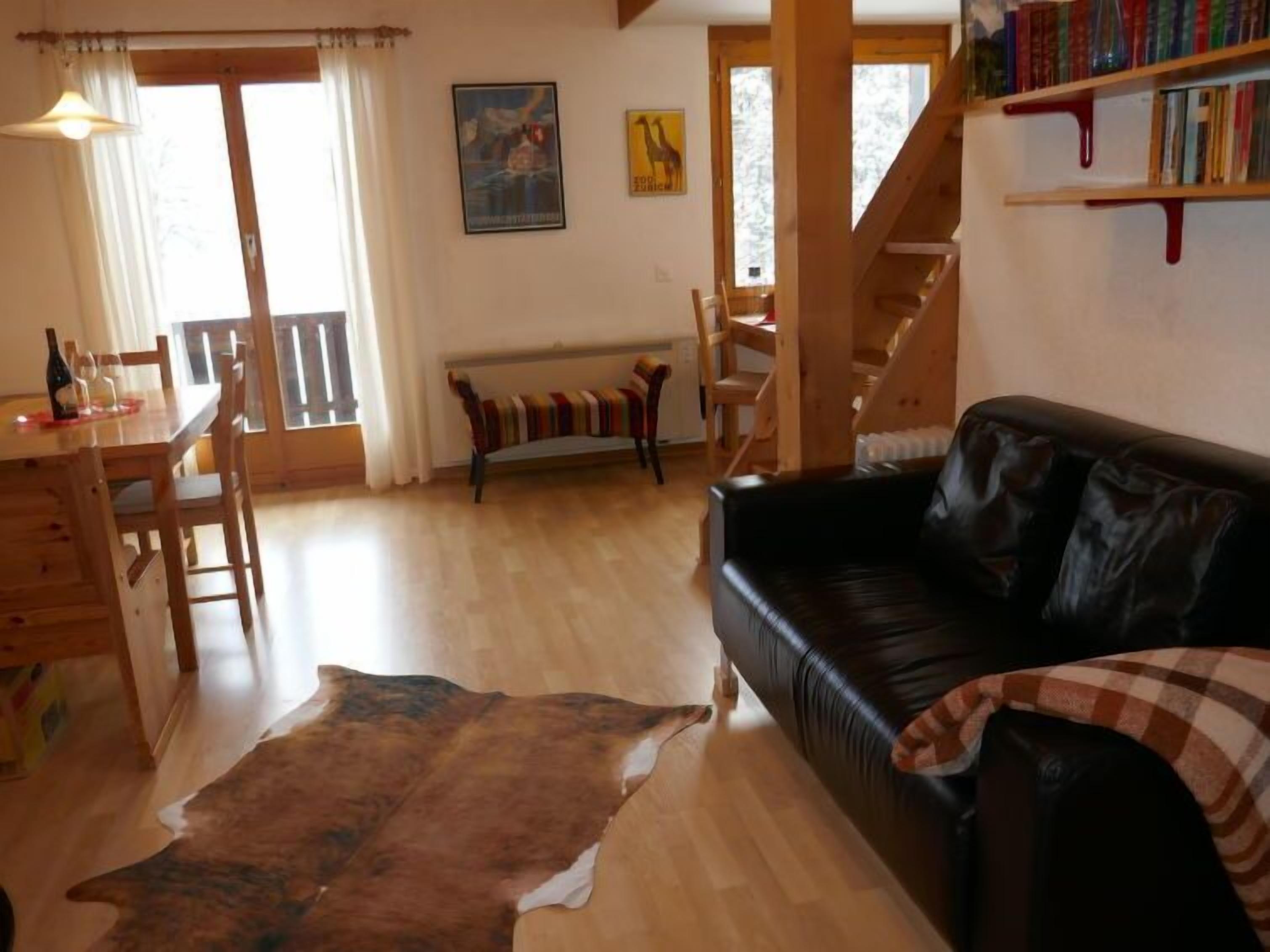 En hyggelig stue med et træspisebord, en sort lædersofa, en træbænk og en stor måtte.