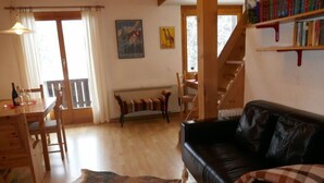 Een gezellige woonkamer met een houten eettafel, een zwarte leren bank, een houten bankje en een groot vloerkleed.