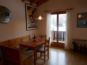 A cozy dining area with a wooden table and benches, a hanging light fixture, and a large window with curtains.