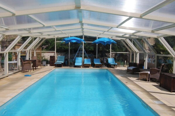 A covered swimming pool with lounge chairs and umbrellas.