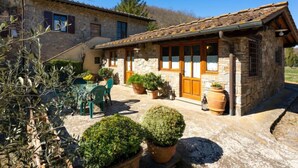 A stone house with a tiled roof, a patio with chairs and potted plants, and a clear blue sky. - Casa Mario by Interhome (Greve in Chianti)