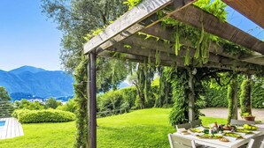 Un área de comedor al aire libre cubierta con una mesa dispuesta para dos, rodeada de abundante vegetación y vistas a montañas.