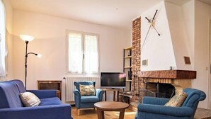 Ein Wohnzimmer mit blauen Sofas, einem Fernseher, einem Kamin und einer Lampe.