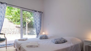 Ein Schlafzimmer mit einem großen Bett, einem Sessel, einem Nachttisch und Blick auf Grün.