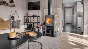 A modern living room with a fireplace, a TV mounted on the wall, and a kitchen area in the background. - Vacation home Solbu by Interhome (Eikerapen)