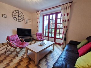 A living room with a TV, two striped chairs, a sofa, and a large window with curtains.
