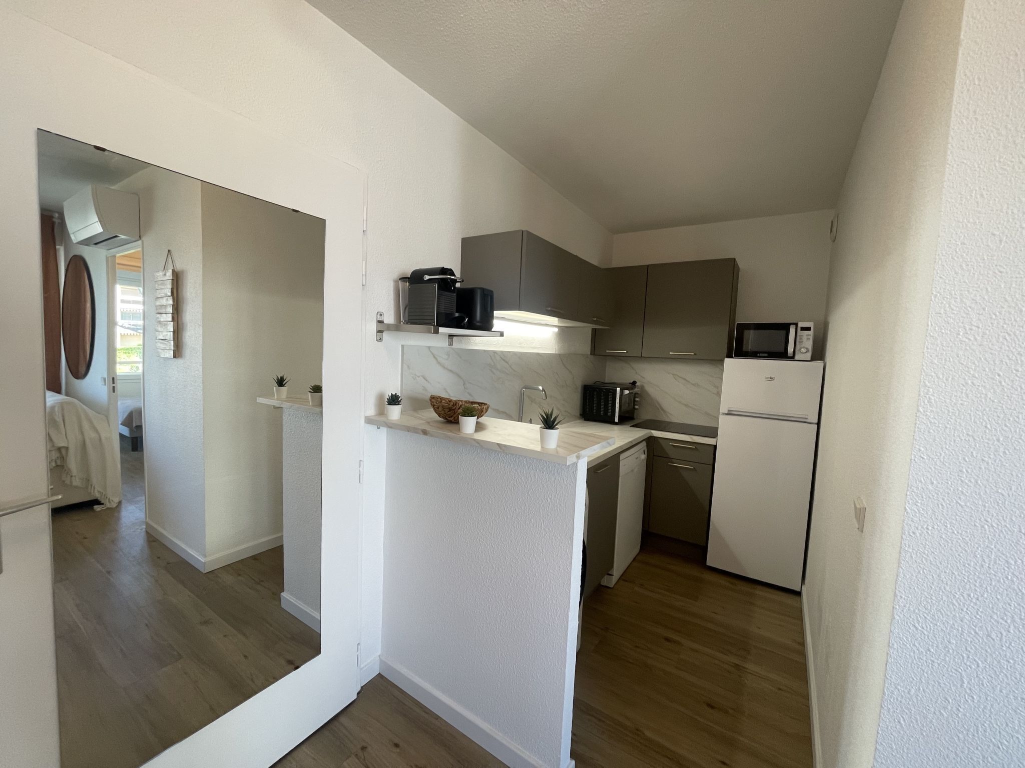 Cocina funcional con armarios blancos, microondas y refrigerador. Hay una pequeña encimera con un tazón y plantas en macetas.