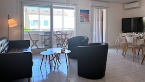 Een moderne woonkamer met een bank, stoelen, een tafeltje, een televisie en een balkon met uitzicht op gebouwen.