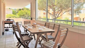 Een balkon met een houten tafel en stoelen, een klein tafeltje met een spel, en uitzicht op bomen en gebouwen.