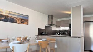 Een moderne keuken met een centraal eiland, roestvrijstalen apparatuur en een eethoek met houten stoelen en een witte tafel.