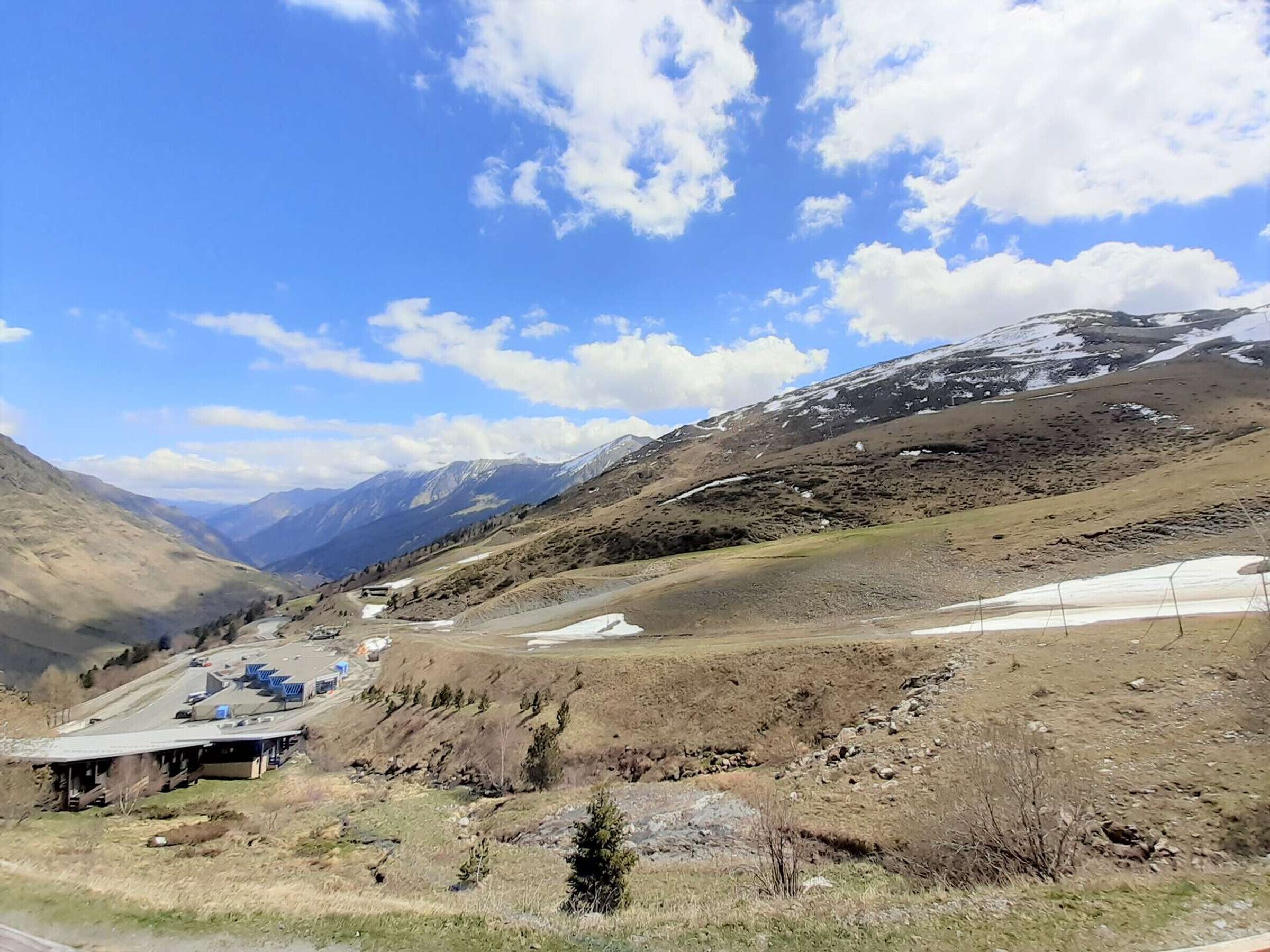 Un paisaje montañoso con un edificio de techo inclinado y un pequeño estacionamiento.