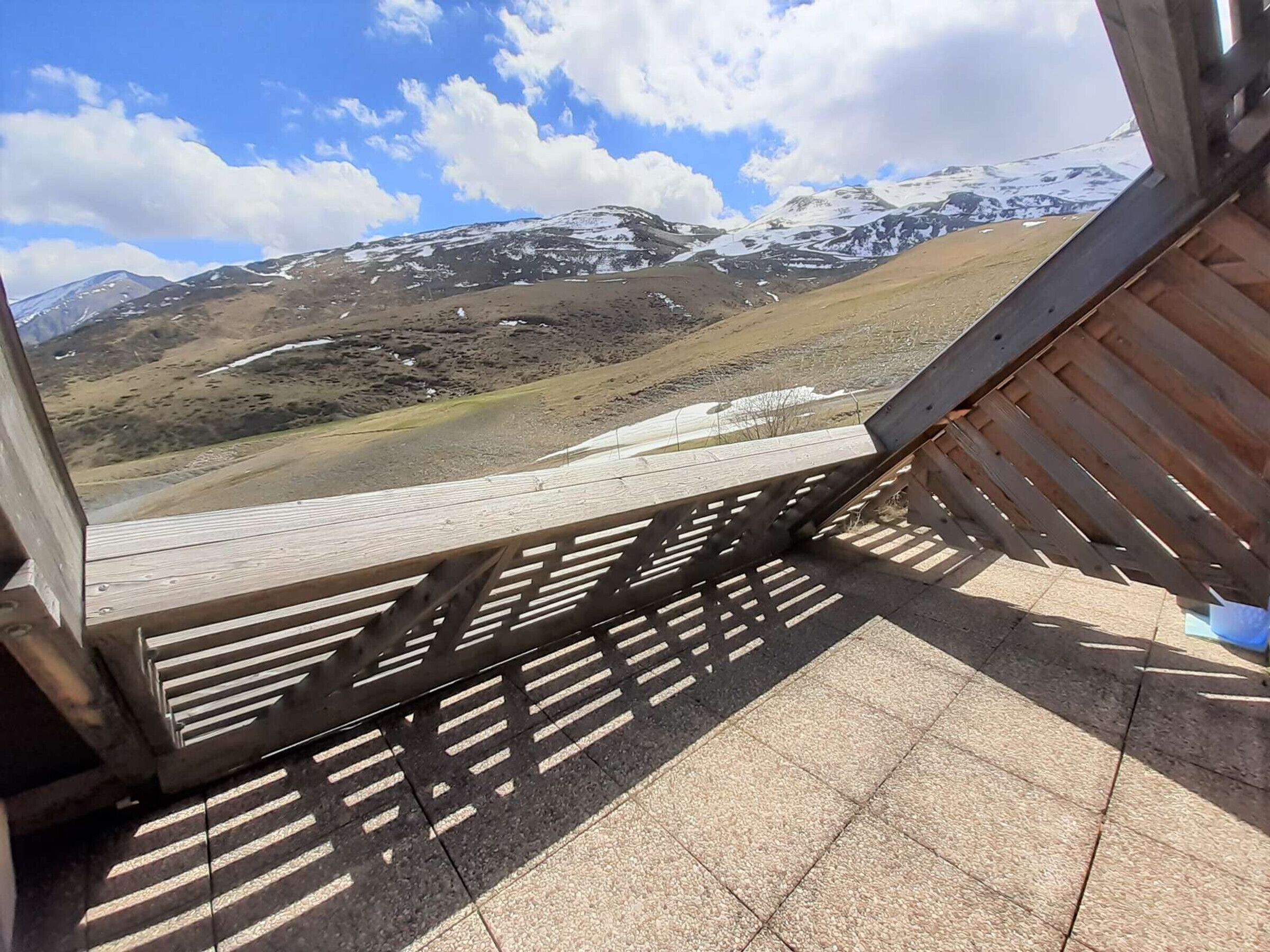 Una terraza de madera con vistas a montañas nevadas y un cielo despejado.