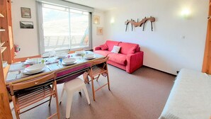 A room with a dining table set for four, a red sofa, and a window with a view. - Cozy Studio for 6 with Mountain View, Ski Locker, and Modern Amenities in Piau-Engaly (Piau-Engaly)