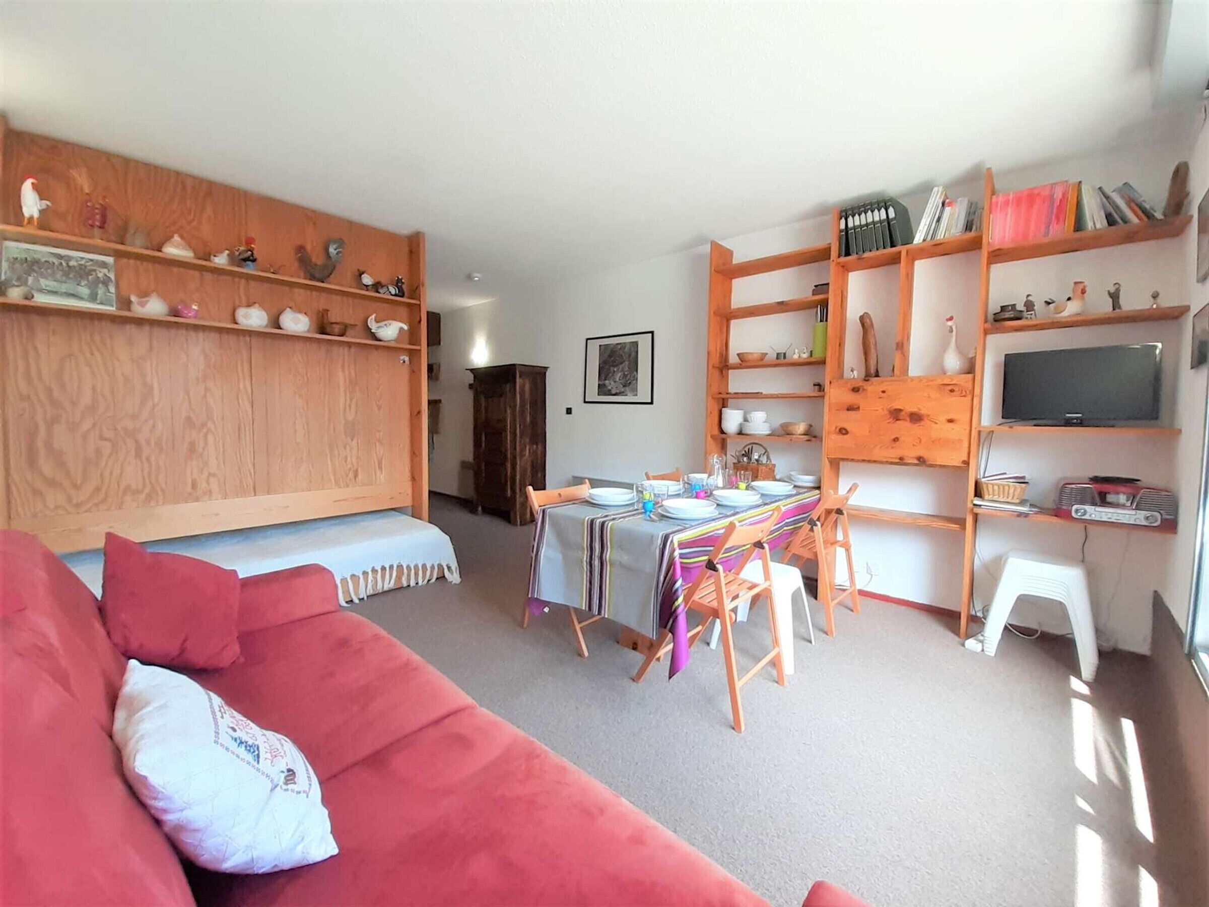 Una sala de estar acogedora con un sofá rojo, estanterías de madera, una mesa de comedor con sillas y un televisor.