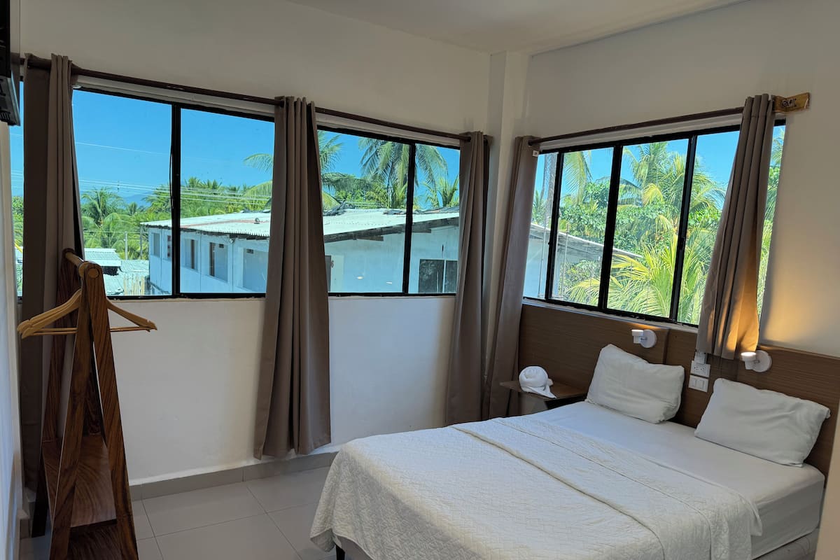A hotel room with a bed, a wooden hanger, and windows with curtains.