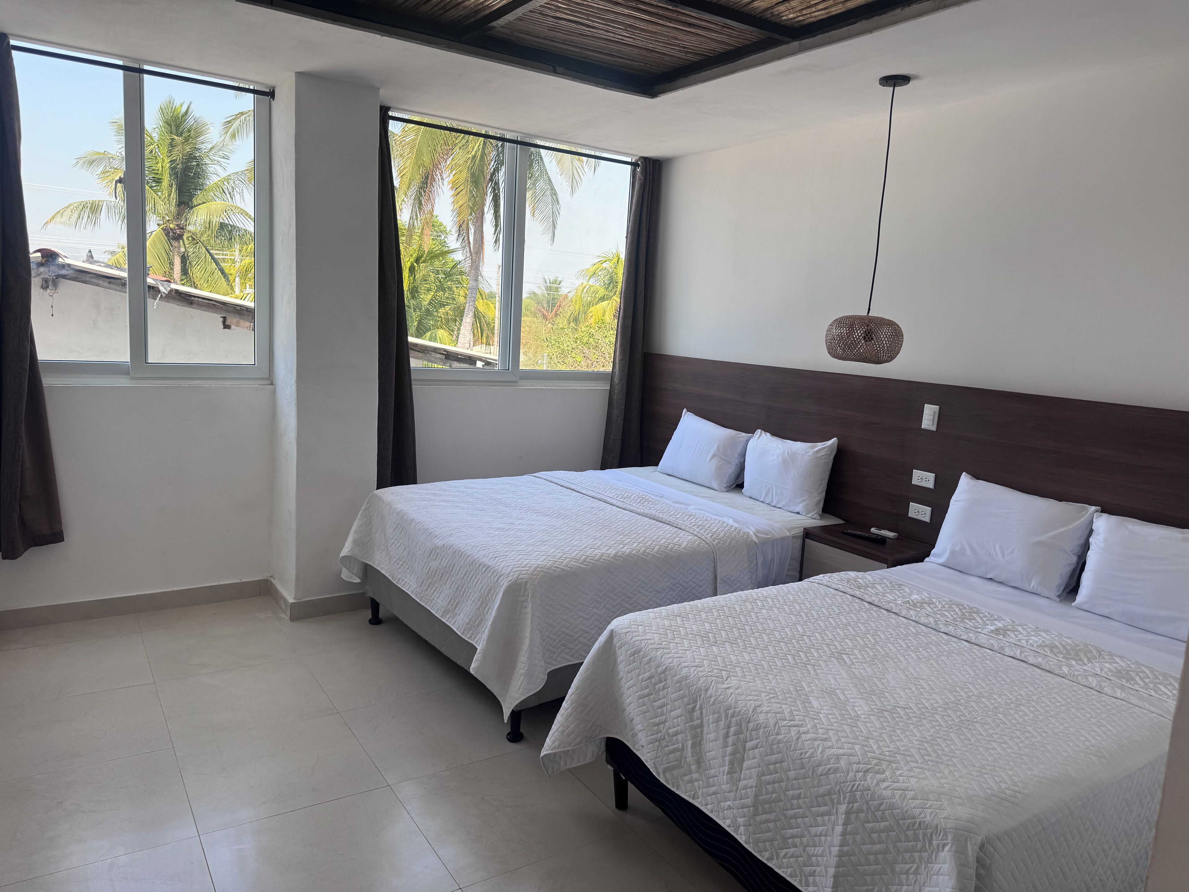 Une chambre d’hôtel avec deux lits, une grande fenêtre et une vue sur les palmiers.
