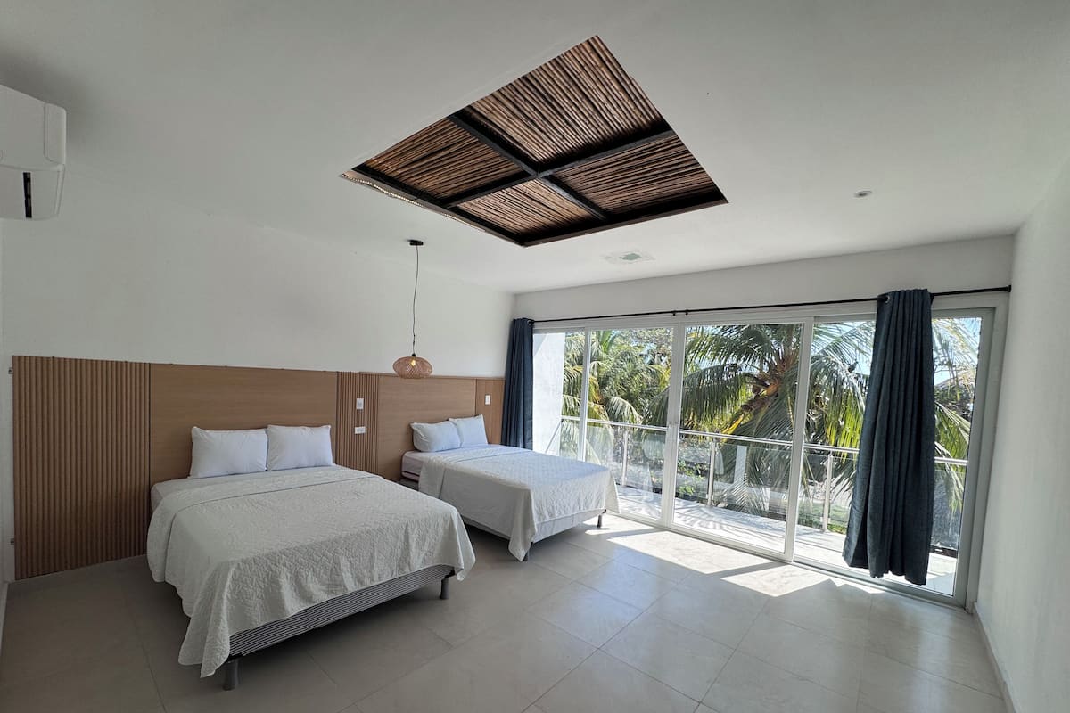 A modern hotel room with two beds, a large window with a view of palm trees, and a ceiling with a wooden panel design.