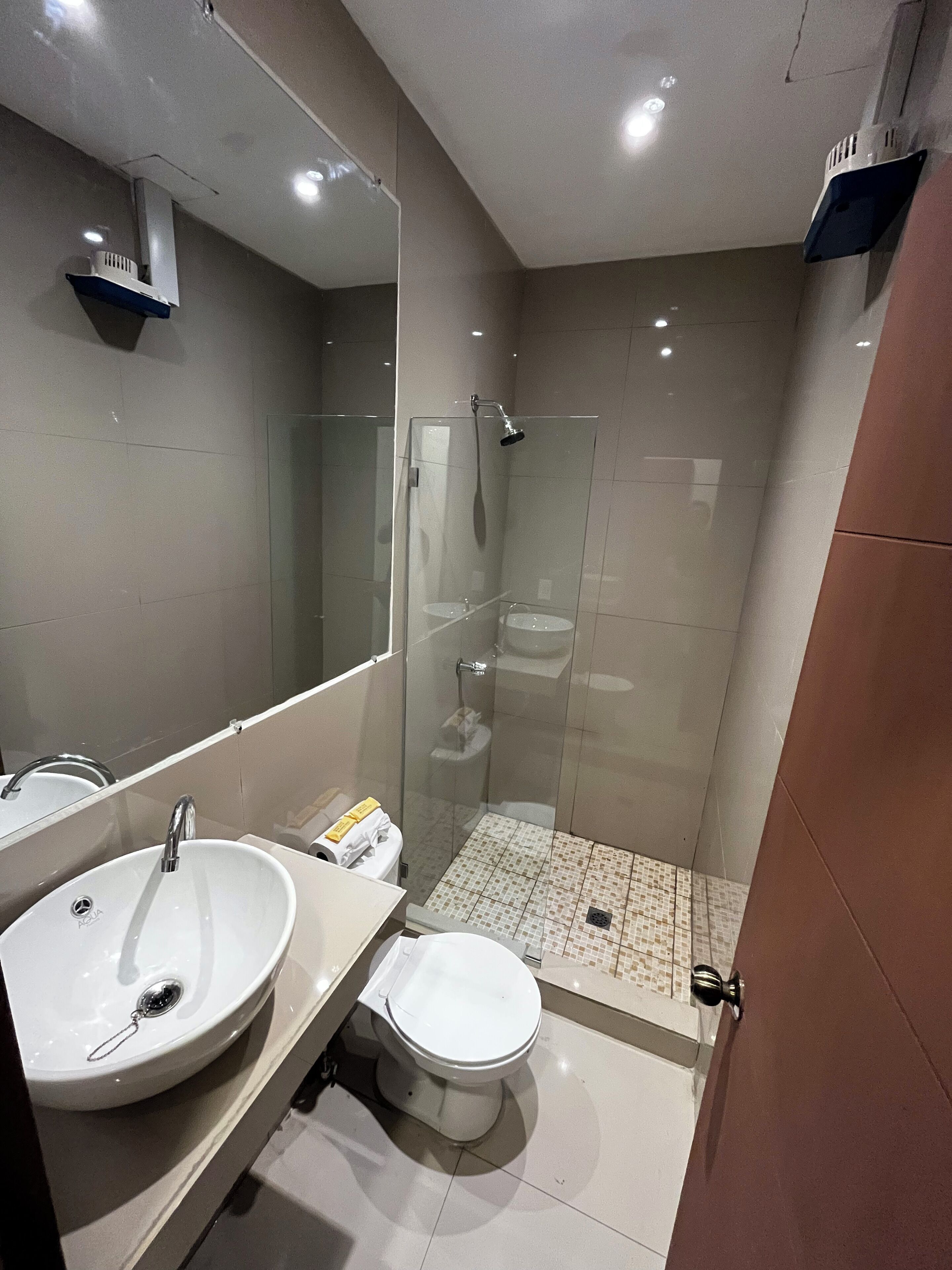 A modern bathroom with a large mirror, a sink, a toilet, and a glass-enclosed shower.
