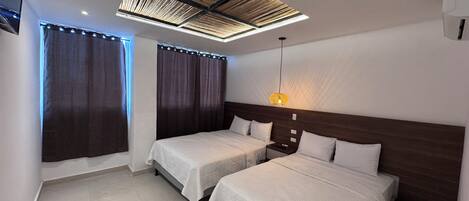 Habitación de hotel con dos camas, un diseño moderno en el techo y una lámpara colgante.