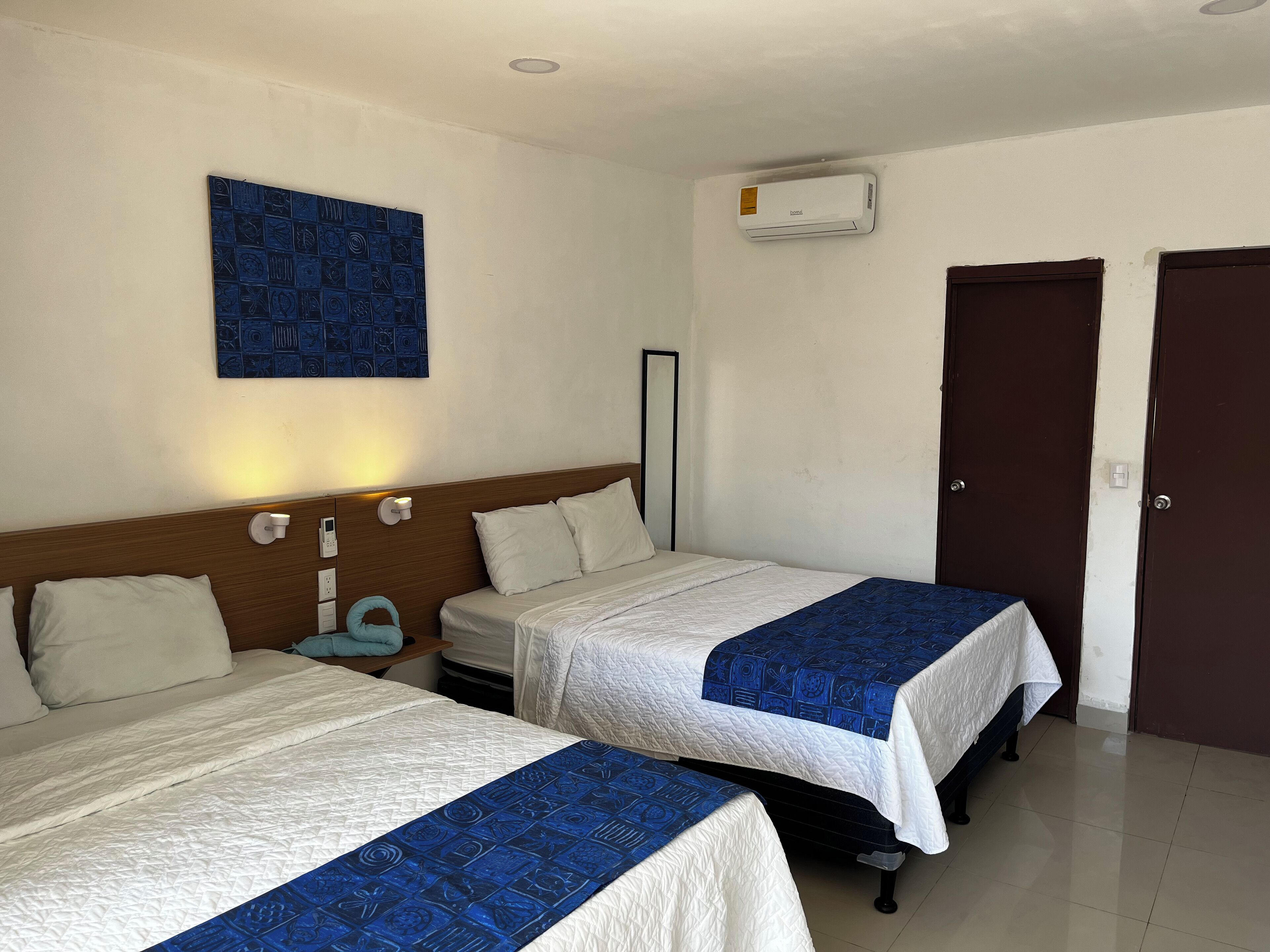 Una habitación de hotel con dos camas, aire acondicionado de pared, una obra de arte azul y una puerta.
