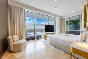 A modern hotel room with a large bed, a TV, a sofa, and a balcony with a city view.